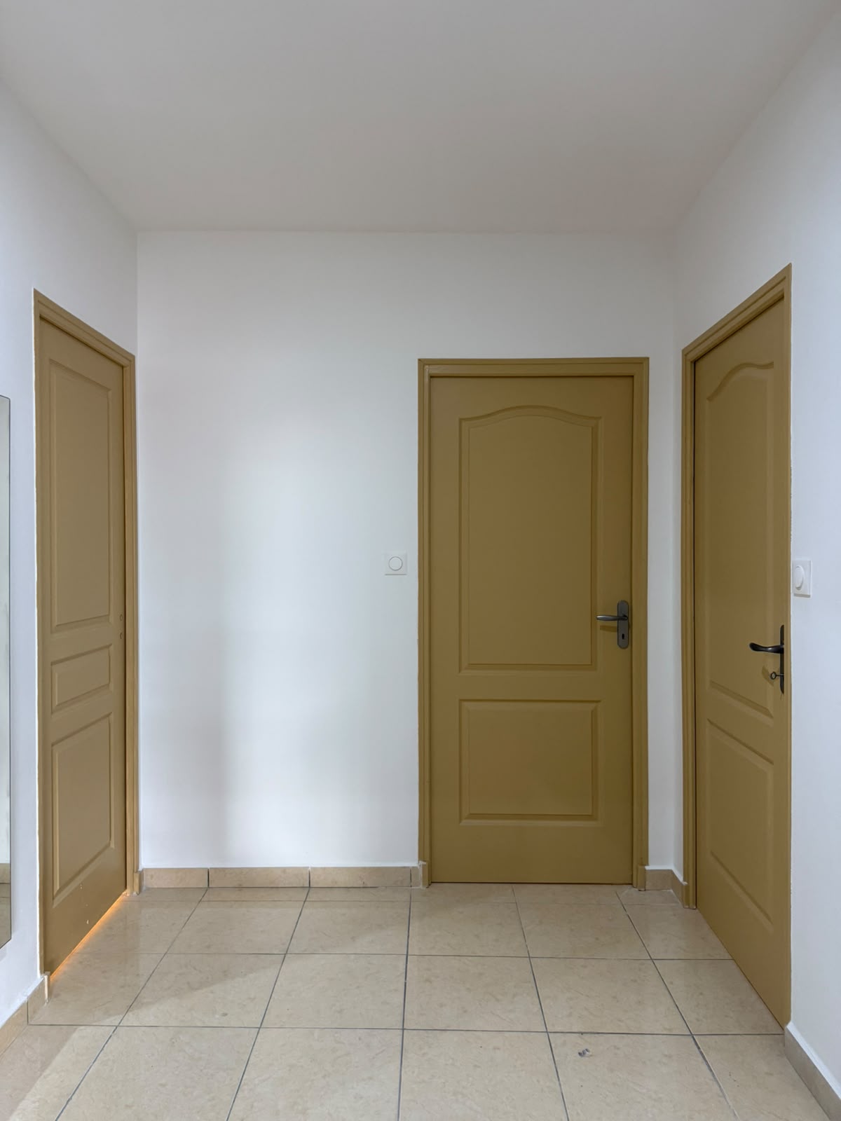Dégagement desservant trois portes ocre, murs blancs et sol carrelé propre